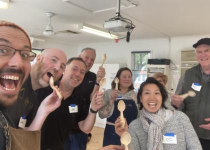 Group of 8 people showing off the spoon they made in class, all smiling. 
