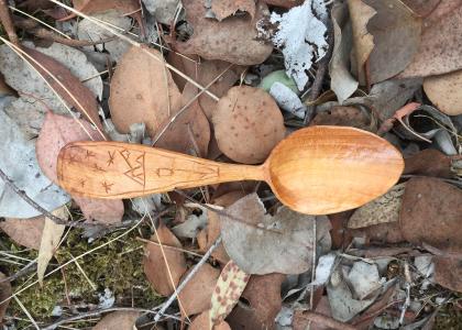 Hand crafted spoon resting on a lush leaf ground covering. 