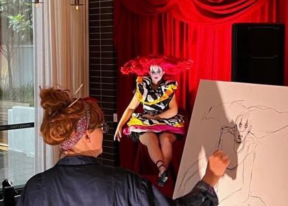 A life drawing student drawing on a large canvas and viewing the life model dressed as a clown. 