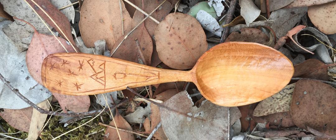 Hand crafted spoon resting on a lush leaf ground covering. 